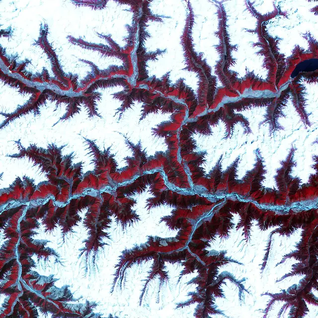 Soaring, snow-capped peaks and ridges of the eastern Himalaya Mountains create an irregular white-on-red patchwork between major rivers in southwestern China