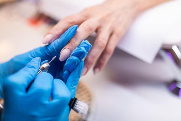 Manicurist doing gel nails at nail salon Close-up of nail technician with blue gloves removing cuticle on client’s long nails with nail drill machine gel polish stock pictures, royalty-free photos & images