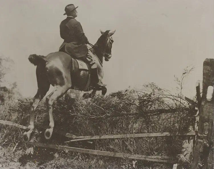 Photograph showing Theodore Roosevelt horseback riding, jumping over a fence.